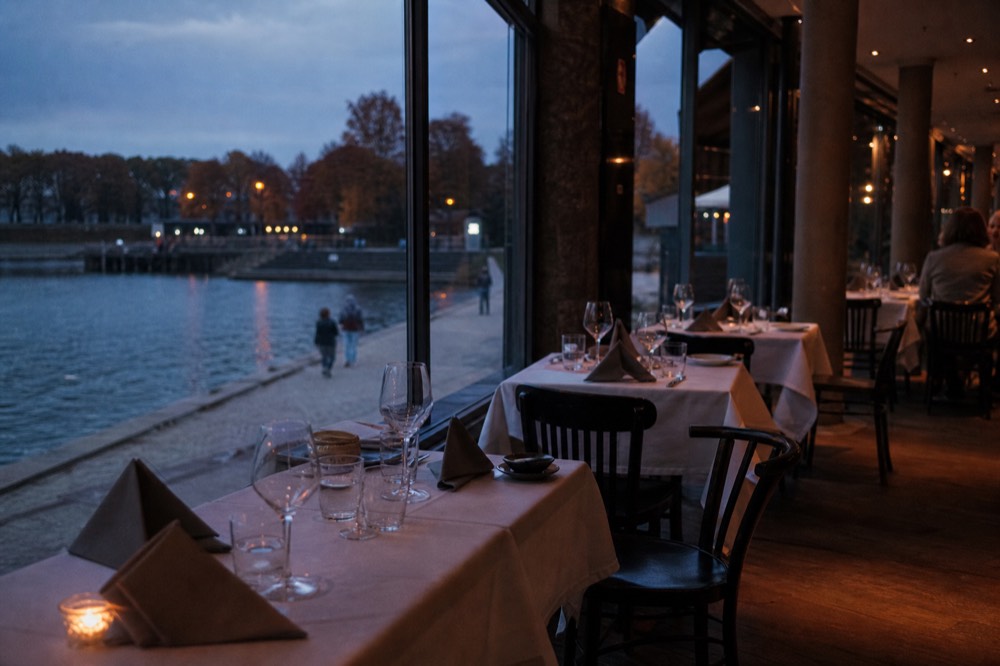 Set dinner tables beside panoramic windows on an evening Seine cruise, no text, no logos, no people