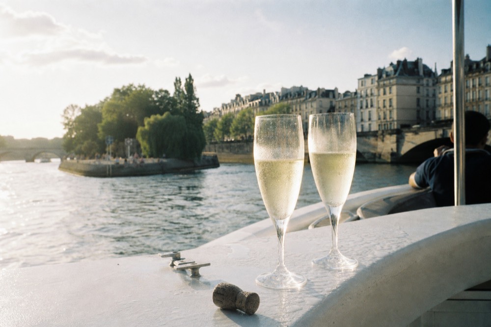 Champagne glasses on a boat rail with the Seine and Paris rooftops beyond, no text, no logos, no people