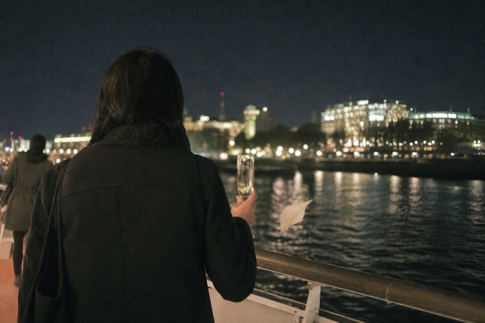 Passenger in a jacket holding a Champagne flute on a boat deck at night, no text, no logos, no people.