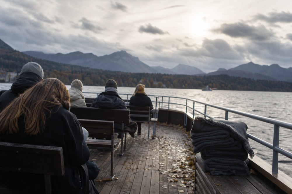 Coats and scarves on passengers seated on an open boat deck in autumn, no text, no logos, no people.