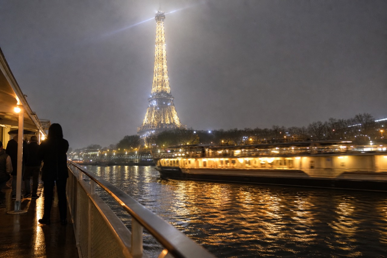 Evening view of an illuminated Seine river boat passing the Eiffel Tower, no text, no logos, no people.