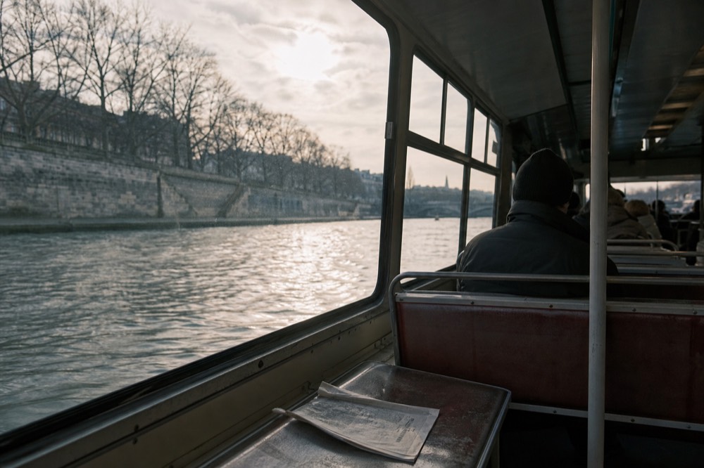 Batobus interior with bench seating and large windows showing the Seine, no text, no logos, no people