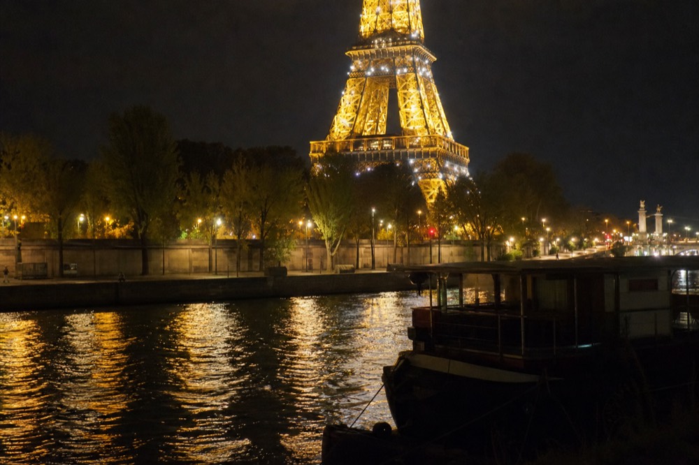 The Eiffel Tower mid-sparkle seen from the water with city lights reflecting on the Seine, no text, no logos, no people.