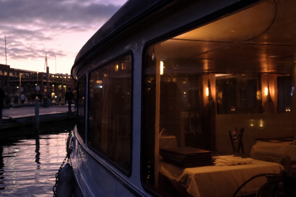A dinner cruise boat with warm interior lighting moored on the Seine at twilight, no text, no logos, no people