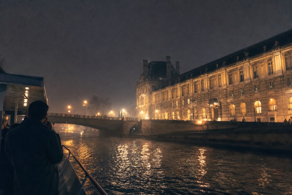 Night view of the Louvre and Seine bridges from a boat deck, no text, no logos, no people