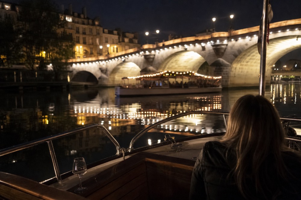 A small illuminated boat passing lit bridges on the Seine at night, no text, no logos, no people