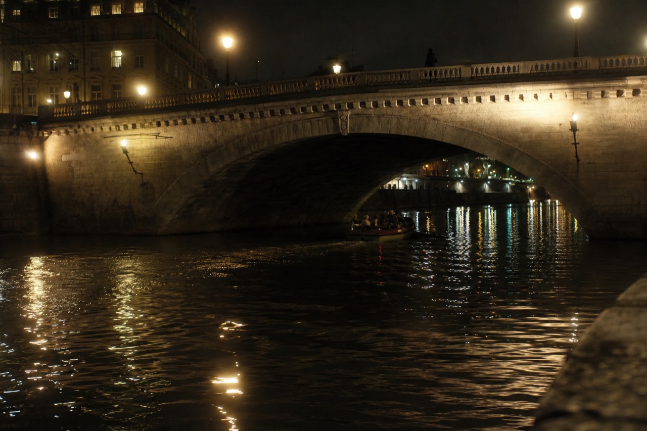 A boat cruising past illuminated Paris bridges on the Seine at night, no text, no logos, no people.