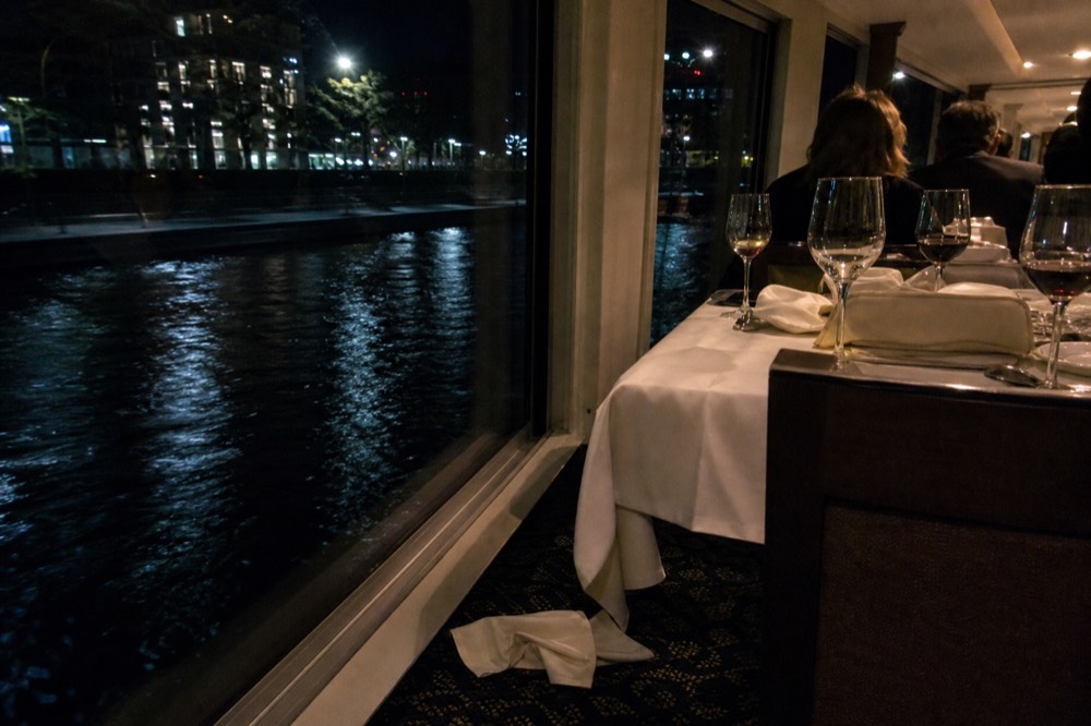 Set dinner table with wine glasses beside a window overlooking the Seine at night, no text, no logos, no people