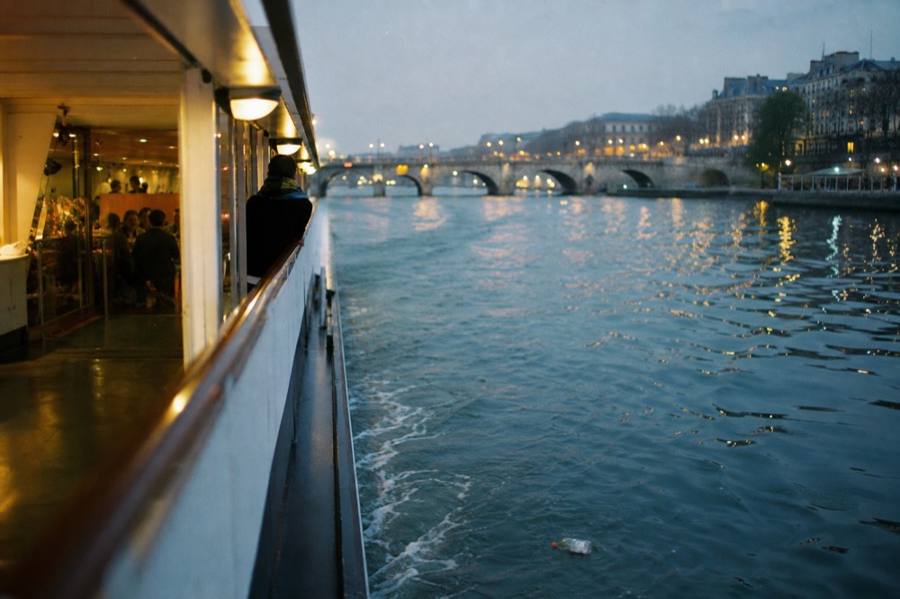 The Seine at dusk with a cruise boat's lights reflecting on the water near illuminated bridges, no text, no logos, no people