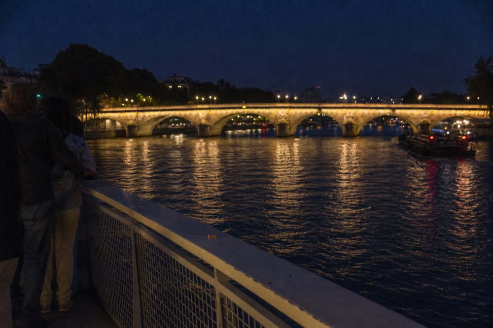 Illuminated Parisian bridges reflecting in the Seine at night from a boat deck, no text, no logos, no people