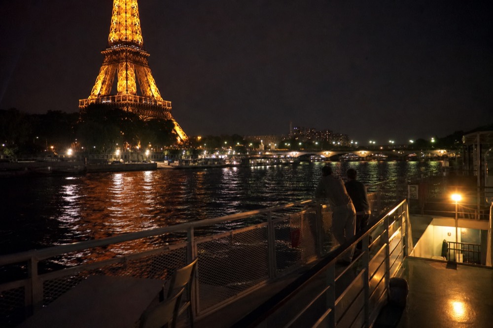 A cruise boat passing the illuminated Eiffel Tower at night on the Seine, no text, no logos, no people
