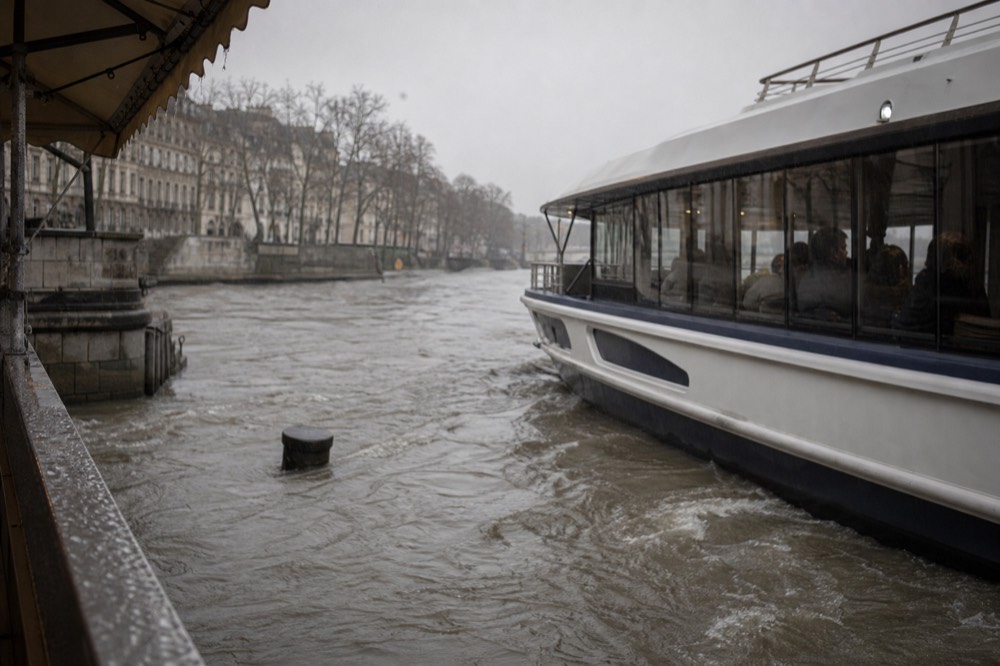 A Seine cruise boat on a rain-grey river passing Parisian quays, no text, no logos, no people