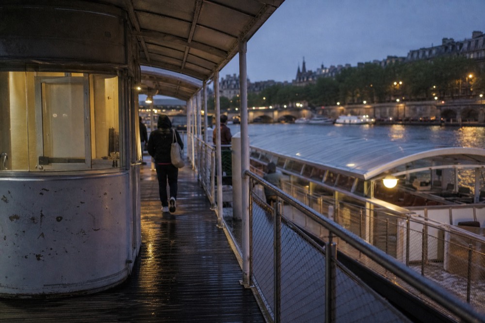 Ticket pontoon on a Paris quay with a moored passenger boat at dusk, no text, no logos, no people