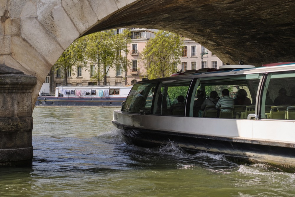A glass-sided sightseeing boat passing ornate Parisian bridges on the Seine, no text, no logos, no people