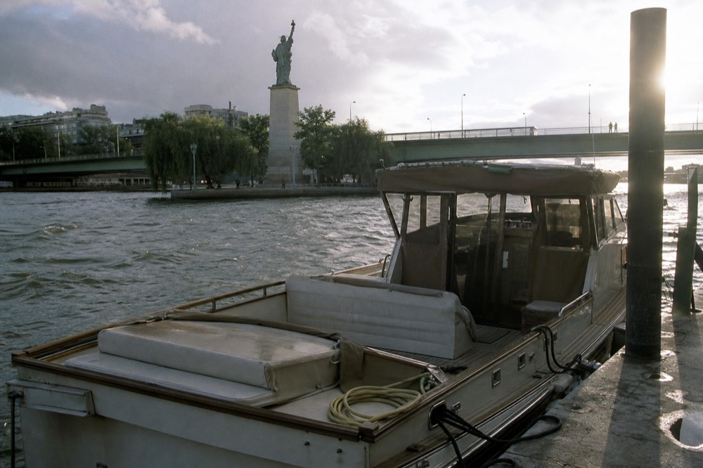 A small private boat moored on the Seine near the Statue of Liberty replica in Paris, no text, no logos, no people