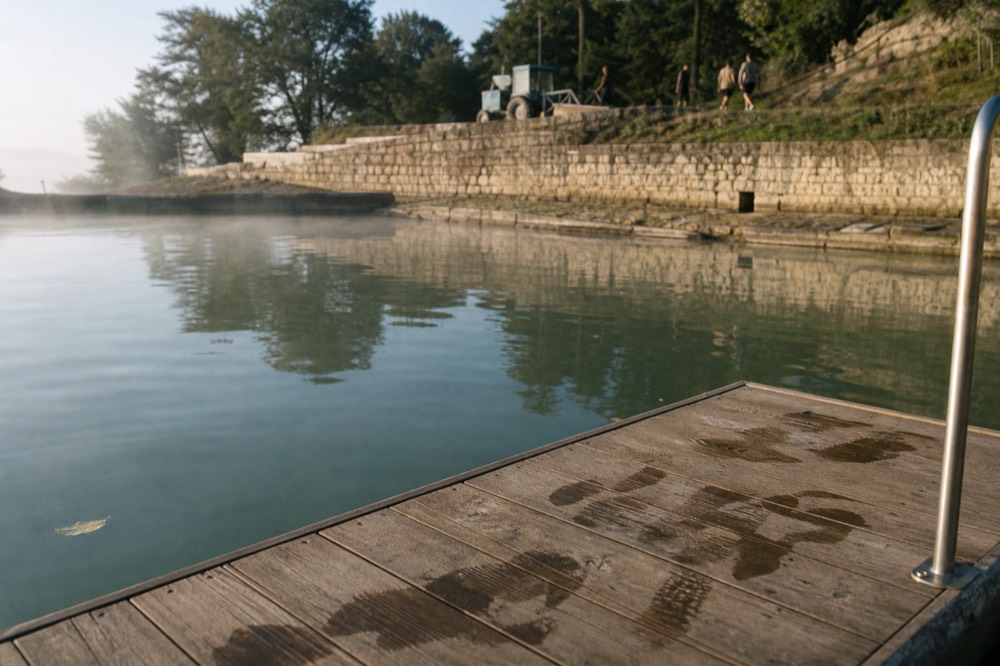 Calm green water of the Seine at a bathing area with a stone quay behind, no text, no logos, no people