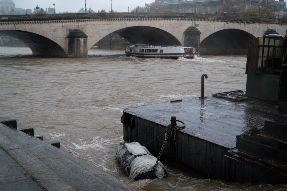 High murky water under a Paris bridge with a passenger boat passing, no text, no logos, no people