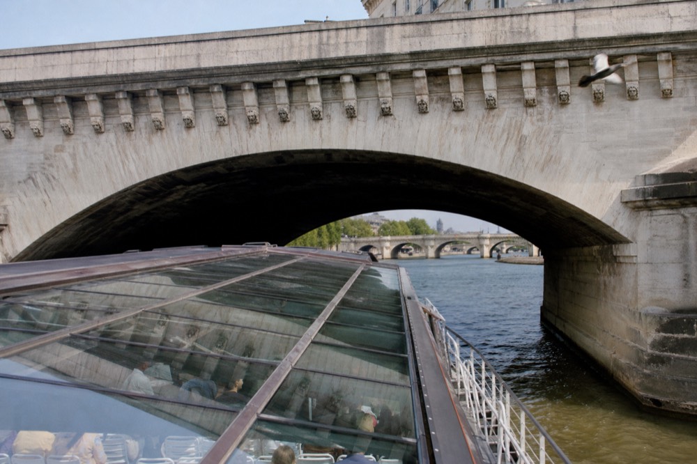 A glass-roofed sightseeing boat passing under a Paris bridge on the Seine, no text, no logos, no people