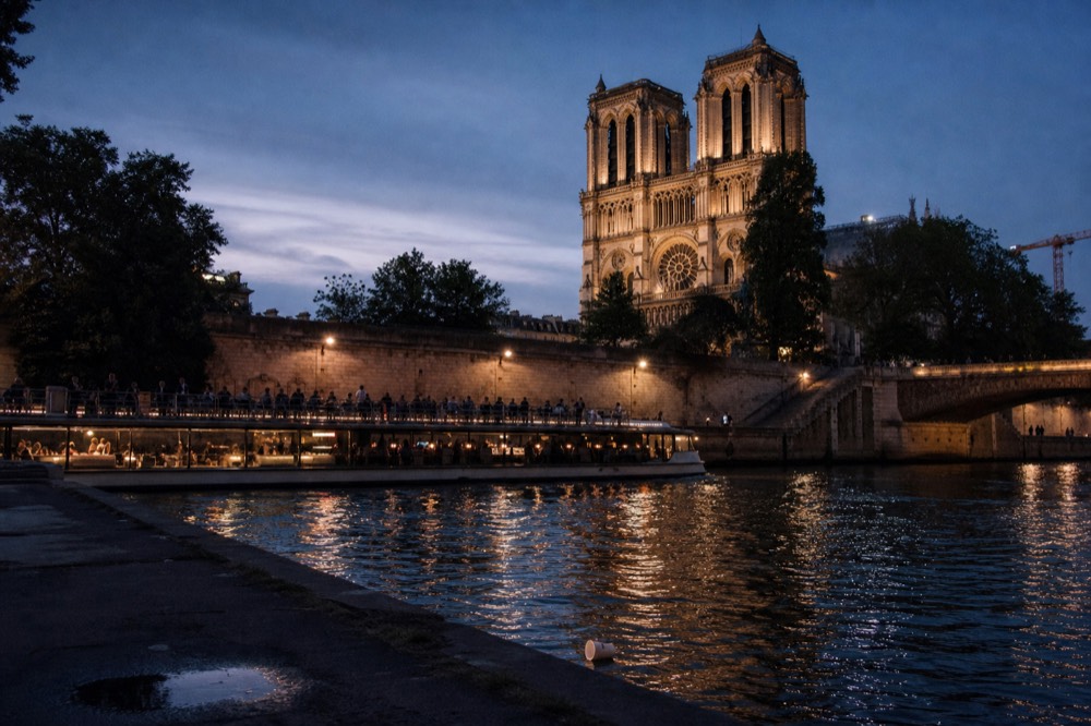 A cruise boat passing the illuminated Notre-Dame Cathedral towers on the Seine at dusk, no text, no logos, no people