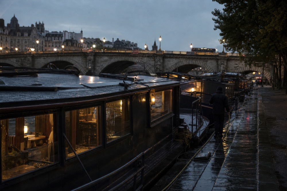 River cruise boats moored at dusk near a lit Paris bridge, no text, no logos, no people