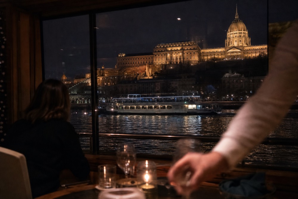 Dinner cruise boat with lit windows gliding past the illuminated Louvre at night, no text, no logos, no people